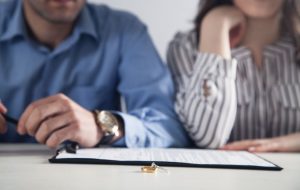 2 people sitting at a table with wedding rings and a document 