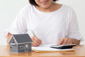 Woman sitting at a table with a calculator, documents and a model house