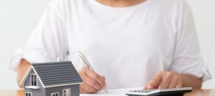 Woman sitting at a table with a calculator, documents and a model house