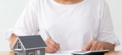 Woman sitting at a table with a calculator, documents and a model house